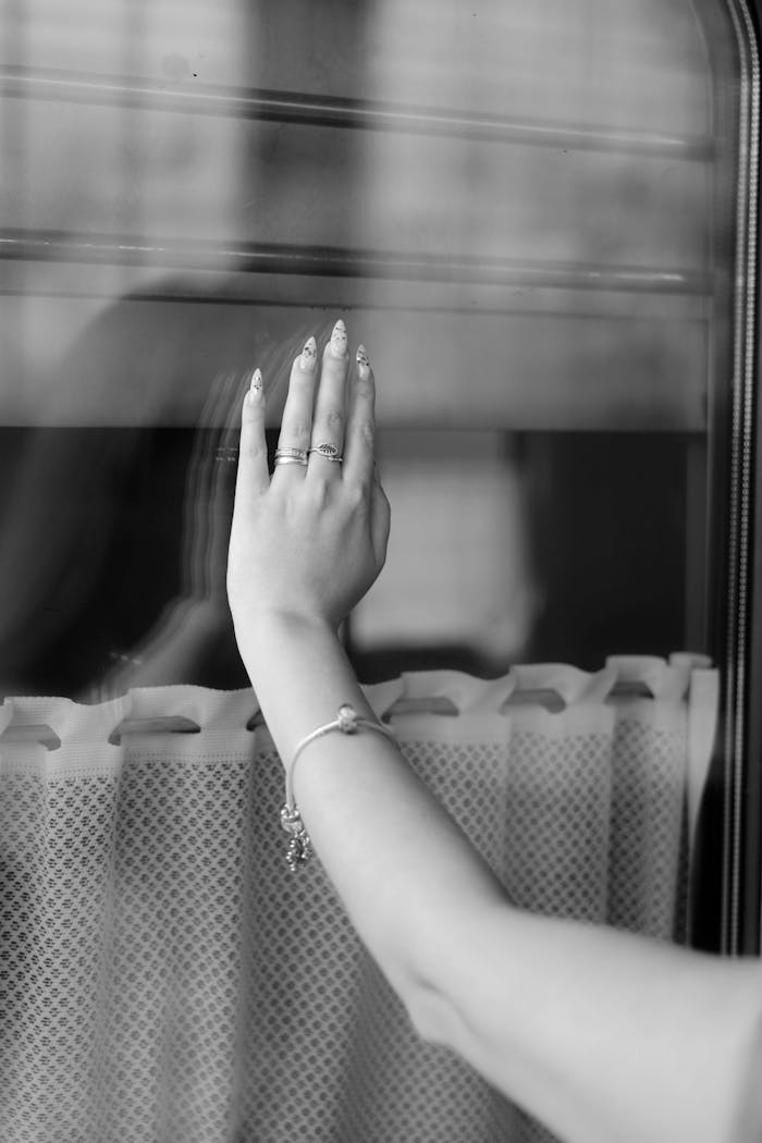 our-services-2 A woman's hand with rings and a bracelet touching a glass window with a curtain.